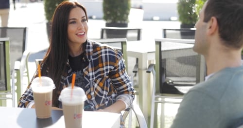 Woman Talks to Man at Outdoor Cafe Table