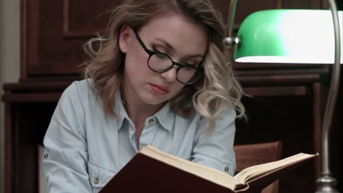 Ernsthafte junge Frau mit Brille auf der Suche nach Informationen im Buch