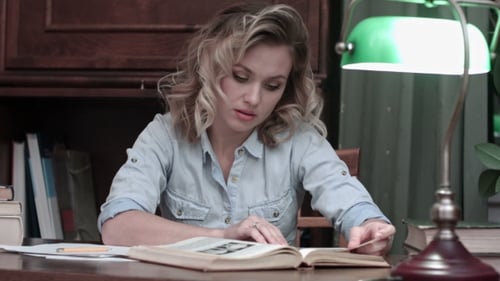 Junge Frau studiert nachdenklich das Buch auf ihrem Schreibtisch