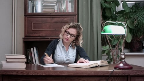 Jeune étudiant en lunettes assis à une table et écrivant des notes d'un livre