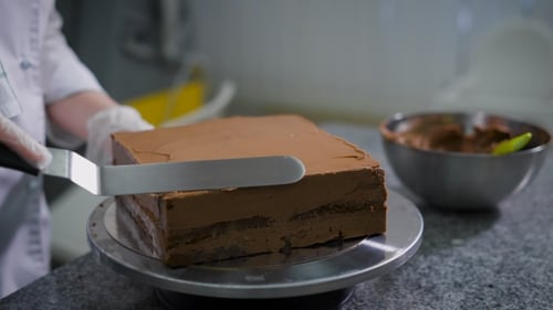 Kitchen in a Candy Store. The Woman in Kitchen Cooks Chocolate Cake. The Confectioner in Gloves and