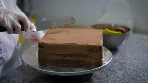 Pastry Chef Metal Spatula Smears Chocolate on Chocolate Sponge Cake, Twisting It in a Place Which Is