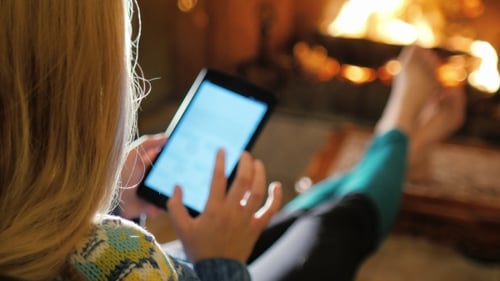 Woman Enjoys the Tablet Near the Fireplace. View Over the Shoulder