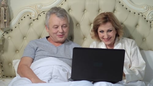 Cheerful Couple Using Laptop Together in Bed