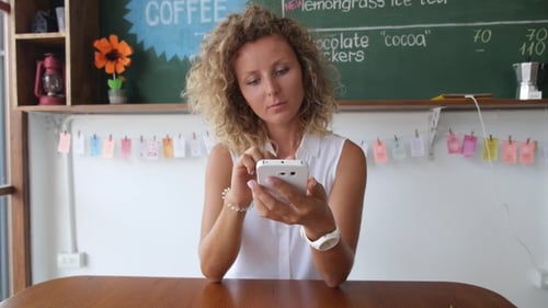 Young Blonde Woman Using Smartphone in Cafe