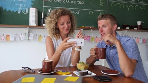Smiling Couple Using Mobile Phone in Coffee Shop
