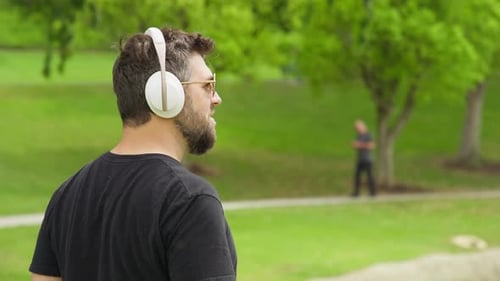 Back View of Handsome Young Man Listening Music in Wireless White Headphones 8K