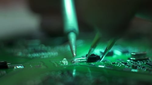 Hands Soldering Component on Green Circuit Board Close Up
