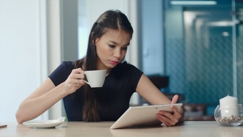 Young Woman Using Digital Tablet While Drinking Coffee or Tea at a Cafe