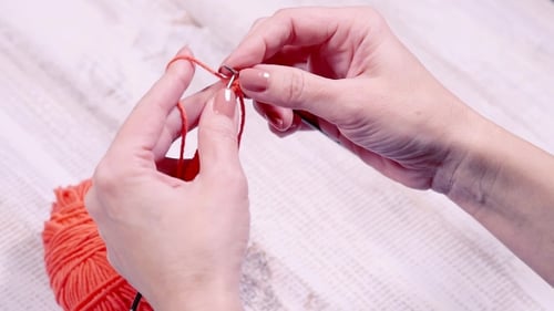 Hands Knitting with Orange Yarn Close Up