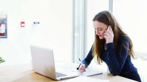 Young Woman Talking on Phone and Writing at Desk