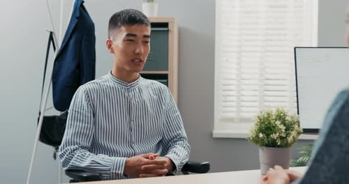 Disabled Man Dressed in Smart Blue Striped Shirt Sits at Desk in Corporate Office in Wheelchair He