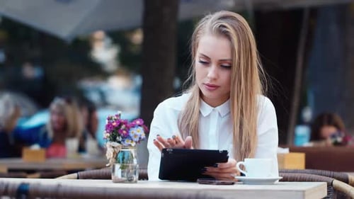 Beautiful Young Woman Uses a Tablet in a Cafe