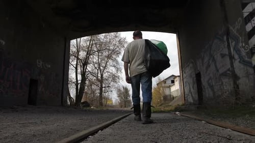 Man Walking on Railroad Tracks Under Overpass