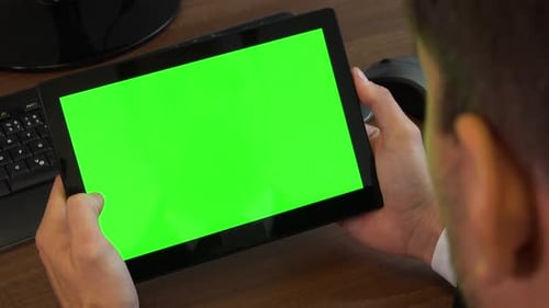 An office worker slides at a tablet with a green screen at a desk with a computer - closeup