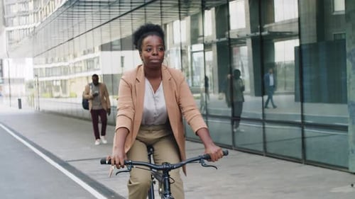 Happy Black Businesswoman Riding Bike along Urban Street