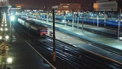 Das Nachtleben eines großen Bahnhofs. Züge kommen an und fahren ab. Schießen im Zeitraffer.