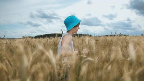 Happy Boy in a Hat Running Across a Golden Wheat Field and Smiling