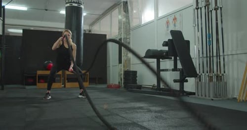 Attraktive Frau trainiert mit Battle Ropes im Fitnessstudio Intensive, fokussierte Frau trainiert schwer