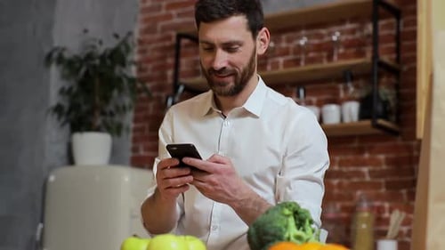 Man Using Phone With Vegetables in Kitchen