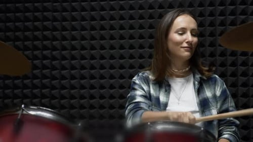 Female drums player is playing on musical instruments in dark modern rehearsal studio.