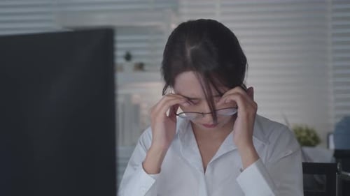 Tired Asian Female Worker Working on desktop computer in the Corporate Office,