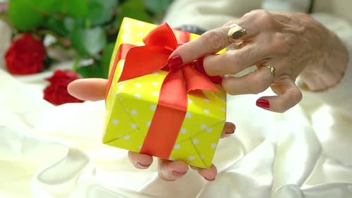 Elderly Hands Holding a Gift with a Red Ribbon