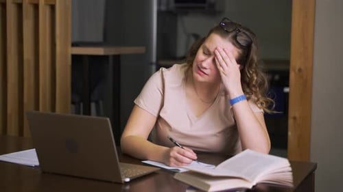 Stressed Woman Writing at Table with Laptop