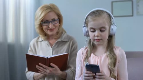 Girl Listens to Phone While Woman Reads Book