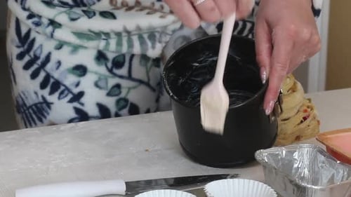 Eine Frau schmiert eine Auflaufform mit Butter. Bereitet Cruffin mit Rosinen und kandierten Früchten
zu