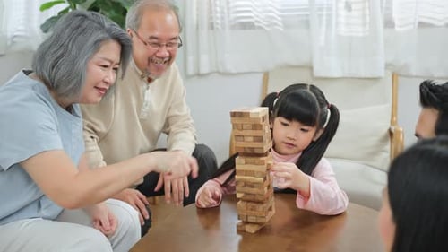 Asian happy family having fun play Tumbling tower wood block game with cute kid daughter at home.