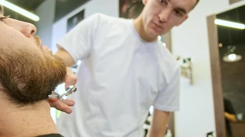 Concentrated Young Man Holds Scissors and Trims Man Beard