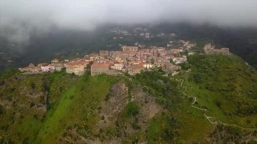 Aerial View Drone Flies Over Medieval Village on Hill Overlooking Misty Mountain Gorge