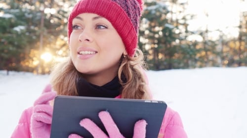 An Attractive Young Woman Enjoys a Tablet or in Snowy Forest Park
