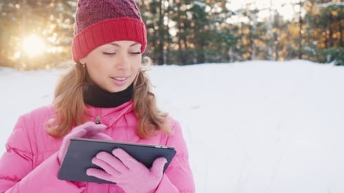 Technology Outdoors. Woman Enjoys the Tablet in a Winter Park at Sunset