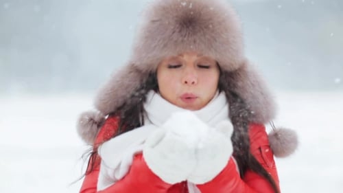 Woman Blowing Snow from Mittens in Winter Landscape