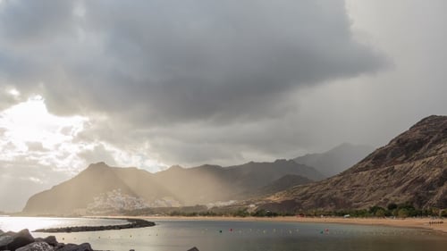 Atlantic Ocean, Beach and Mountains Behind. From the Clouds Make Their Way Rays of the Sun. .