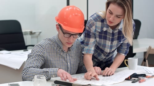 Architecte travaillant sur des plans tandis qu'une collègue apporte plus de dessins