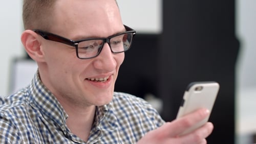 Young Man in Office Laughing at Text Message on Smartphone