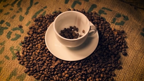 Coffee Beans Overflowing Cup on Burlap Surface