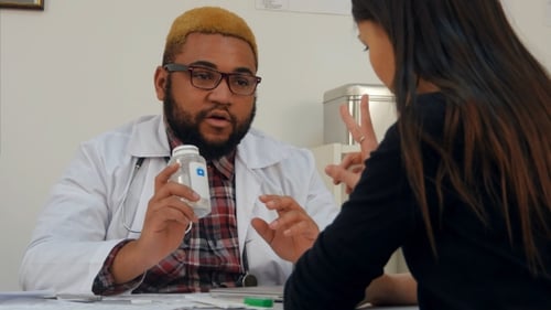 Afroamerican Doctor Prescribing Pills To Female Patient and Explaining Dosage