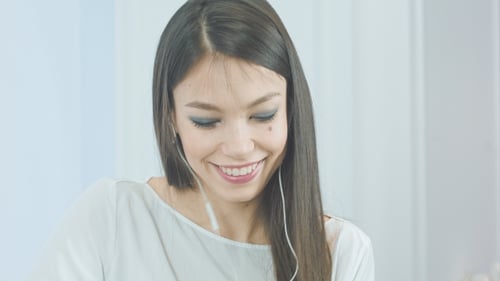 Smiling Young Woman Puts in Wired Earbuds