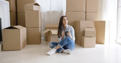 Woman Surrounded by Moving Boxes Smiling in New Home