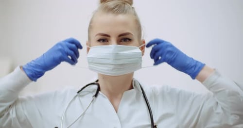 Female Doctor Putting on Protective Mask at Clinic