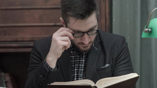 Man Reading Book Indoors Under Lamp