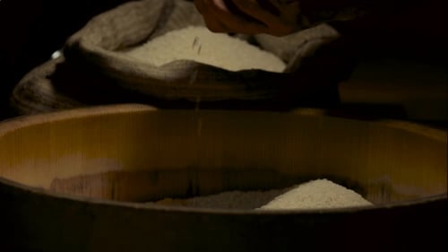 Hands Sifting Rice into Wooden Container