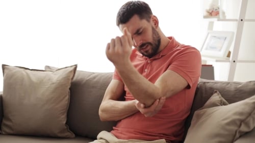 Man Massaging Elbow in Sunny Home