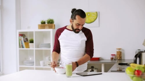 Man Eats Cereal and Uses Tablet in Kitchen
