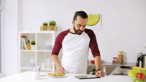 Man Using Tablet and Eating Snack in Kitchen