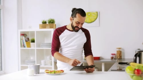Man Using Tablet and Drinking Coffee in Kitchen